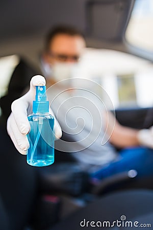 Driver with face mask and medical gloves holding disinfectant spray bottle in car, coronavirus pandemic concept Stock Photo