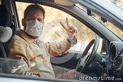 a man driving a car puts on a medical mask during an epidemic, a taxi driver in a mask, protection from the virus Stock Photo