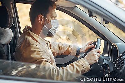 A man driving a car puts on a medical mask during an epidemic, a taxi driver in a mask, protection from the virus Stock Photo