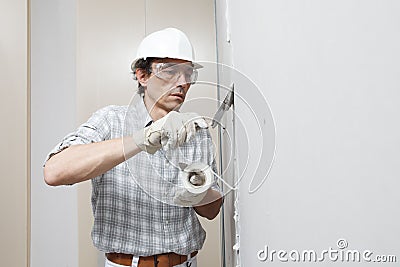 Man drywall worker or plasterer putting mesh tape for plasterboard on a wall using a spatula and plaster. Wearing white hardhat, Stock Photo