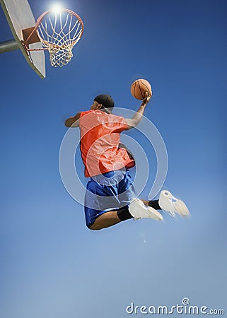 Man Dunking Basketball Into Hoop Against Blue Sky Stock Photo