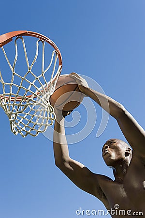 Man Dunking Basketball Into Hoop Against Blue Sky Stock Photo