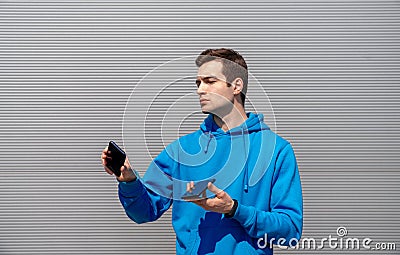 Man with earring holds two smartphones in both hands, look at them with serious face, wearing in blue hoody, black fitness tracker Stock Photo