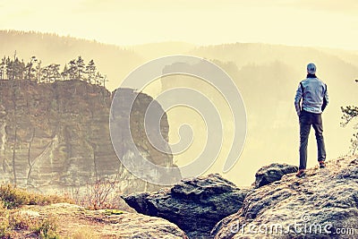 Man on edge of cliff high above misty valley. Travel hiking and Lifestyle. Stock Photo