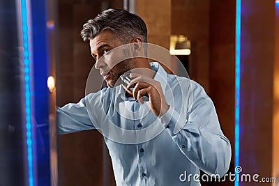 Man With Electric Razor Shaving Face In Bathroom. Men Grooming Stock Photo