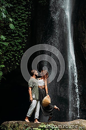 A man embraces a woman at a waterfall. A couple in love at a waterfall. Honeymoon trip. Happy couple in Bali. A beautiful couple Stock Photo