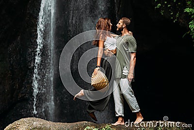 A man embraces a woman at a waterfall. A couple in love at a waterfall. Honeymoon trip. Happy couple in Bali. Stock Photo