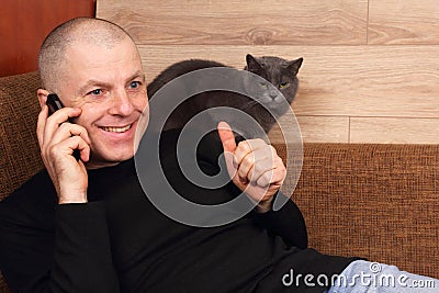 Man emotionally talking on the phone resting on the couch with the cat Stock Photo