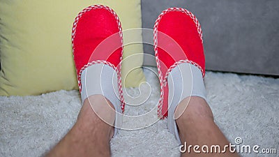 A man enjoys the comfort of home.Legs in red slippers,close-up,sitting on a white carpet. Stock Photo