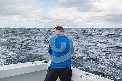 A man in excitement with a spinning in his hands pulls fish from the ocean from the side of the boat.. fishing in Florida. USA. Stock Photo