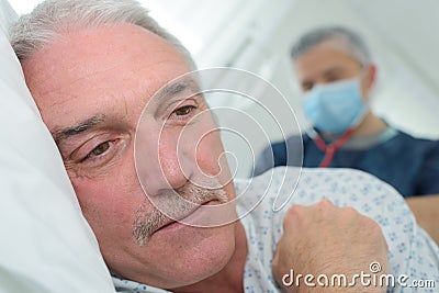 Man face down on bed masked medical worker behind him Stock Photo