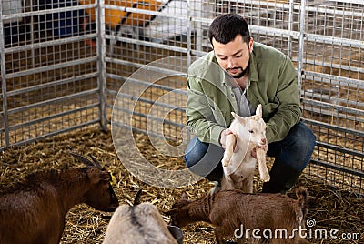 Farmer squatting with goatling in shed Stock Photo