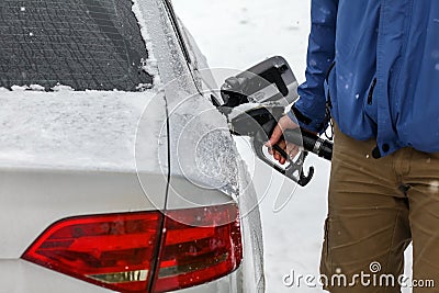 Man filling fuel to his diesel car at gas station in winter. Detail on snow covered tank cover and pump nozzle Stock Photo