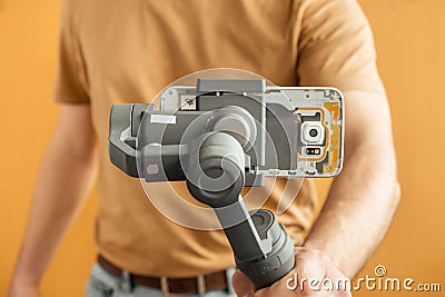 Man filming with a smartphone using a gimbal stabilizer on yellow background. Using three-axis electronic stabilizer to make vlogs Stock Photo