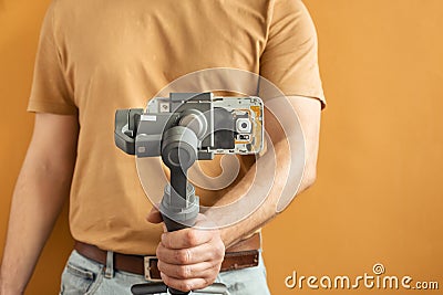 Man filming with a smartphone using a gimbal stabilizer on yellow background. Using three-axis electronic stabilizer to make vlogs Stock Photo