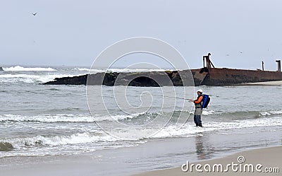 A man fishes in the surf next to a shipwreck in the Salinas River National Wildlife Refuge Editorial Stock Photo