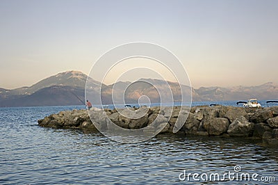 Man fishing on the rocks of the tidal barrier at sunset. Amusement. Stock Photo