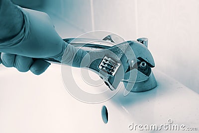 Man fitting repairing tap on a bathroom sink faucet with an adjustable spanner wrench. Stock Photo