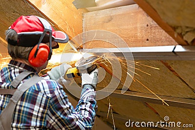 Man fixing metal frame using angle grinder on attic ceiling covered with rock wool Stock Photo