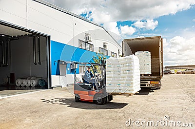 A man on a forklift works in a large warehouse, unloads bags of raw materials into a truck for transportation Stock Photo