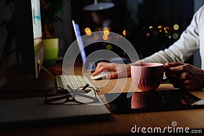 Man freelancer drinking tea while working late at night at computer at home office, remote work Stock Photo