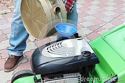 A man fueling a lawn mower. A green lawnmower. Gardening. Maintenance of equipment Stock Photo