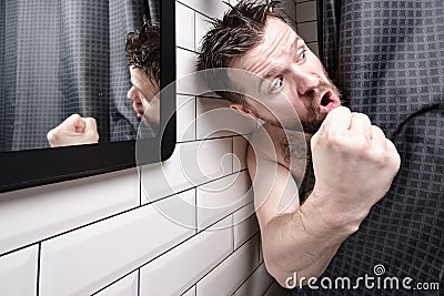 Man is furious, he peeks out from behind a curtain in the shower room, shows fist in anger and yells at someone. Stock Photo