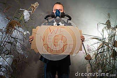 A man in a gas mask in a suit shrouded in smoke is walking in a dangerous radioactive zone with a poster We Need Change Stock Photo