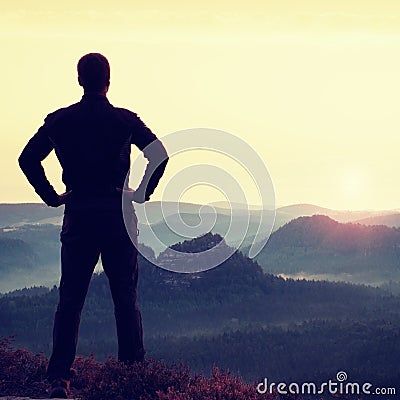 Man gesture triumph. Satisfy hiker in dark sportswear at edge with heather.Tall man on the peak of sandstone cliff watching to lan Stock Photo