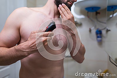 A man is getting ready to shave with a power loom. A man with an athletic figure in the bathroom Stock Photo