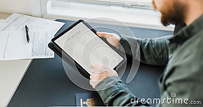 Man getting visa and reading application on tablet, passport on desk. Stock Photo