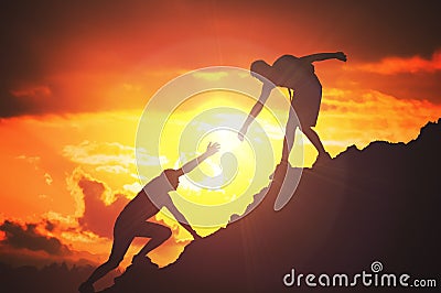 Man is giving helping hand. Silhouettes of people climbing on mountain at sunset Stock Photo