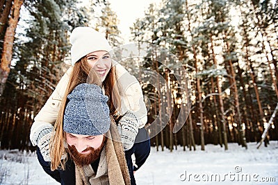 Man giving woman piggybacks ride on winter vacation in a snowy forest Stock Photo