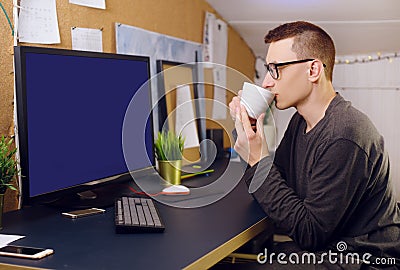 A man with glasses drinks coffee, tea and looks at the green screen. A man works at home. Stay home, freelancer, training Stock Photo