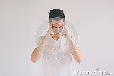 Man with glasses having troubles and headache at home. Young black-haired nerd guy wearing white t-shirt holding hands Stock Photo