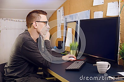 The man in glasses uses the keyboard and the mouse looks at the green screen. A man works at home. Stock Photo