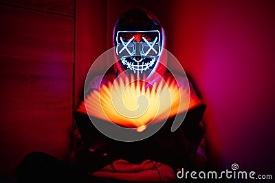 Man in glowing mask sitting in the corner with book-shaped lamp Stock Photo