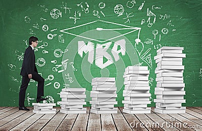 A man is going up using a stairs which are made of white books to reach graduation hat. The written word MBA is drawn on the green Stock Photo
