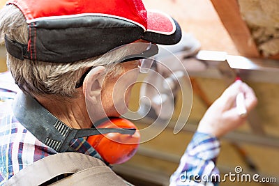 Man in googles making a mark on metal frame on unfinished attic ceiling. Attic insulation and renovation Stock Photo
