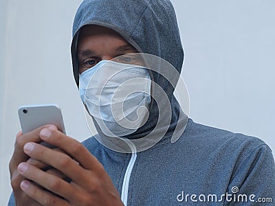 A man in gray hoodie, wearing a mask with cellphone Stock Photo