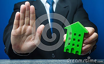 Man with a green house makes a stop gesture. Bank refusal to provide a mortgage loan. Housing problems, unscrupulous dishonest Stock Photo