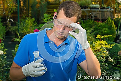 A man in a greenhouse examines a test tube with a liquid for fertilizing plants Stock Photo