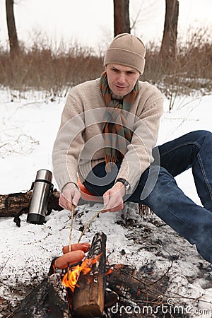 Man grilling sausages at campfire in winter Stock Photo