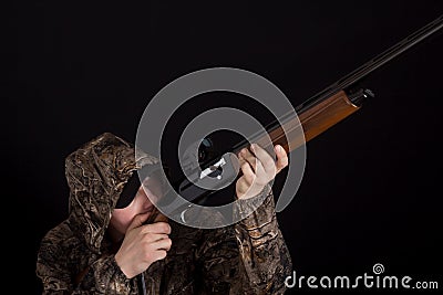 The man with the gun aims. Hunter in camouflage clothes with a shotgun on a black background. Military with weapons. Copy space. Stock Photo