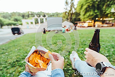 man hand holding beer bottle woman hand holding chips open air cinema Stock Photo