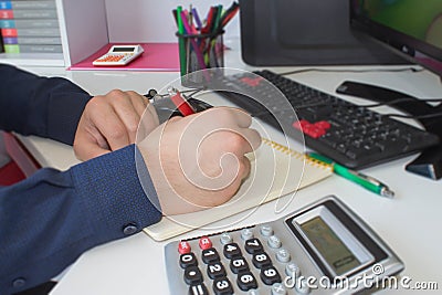 Man hand with pen, calculator and computer on wooden table. He is using his calculator and writing numbers down. Concept of accoun Stock Photo
