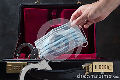 Caucasian man hand stuffing face mask into security briefcase with handcuffs Stock Photo