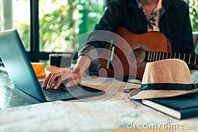 Man` hand use laptop for search holiday reservation. Map, book and hat on the table Stock Photo