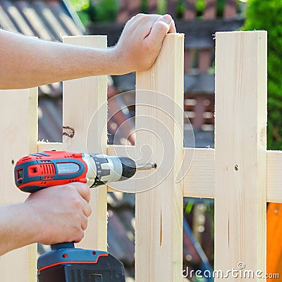 Man hands building wooden fence with a drill and screw. DIY concept. Close up of his hand and tool. Stock Photo