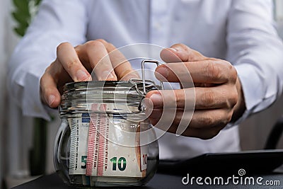 Man hands counting expenses banknotes of euro cash from glass jar in the piggy bank on calculator. Close up of hands Stock Photo